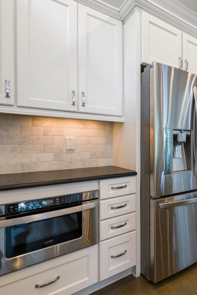 Modern kitchen remodel featuring white cabinets, stainless steel appliances, under-cabinet lighting, and a sleek black countertop installed by Alcord Construction in Middle Georgia.