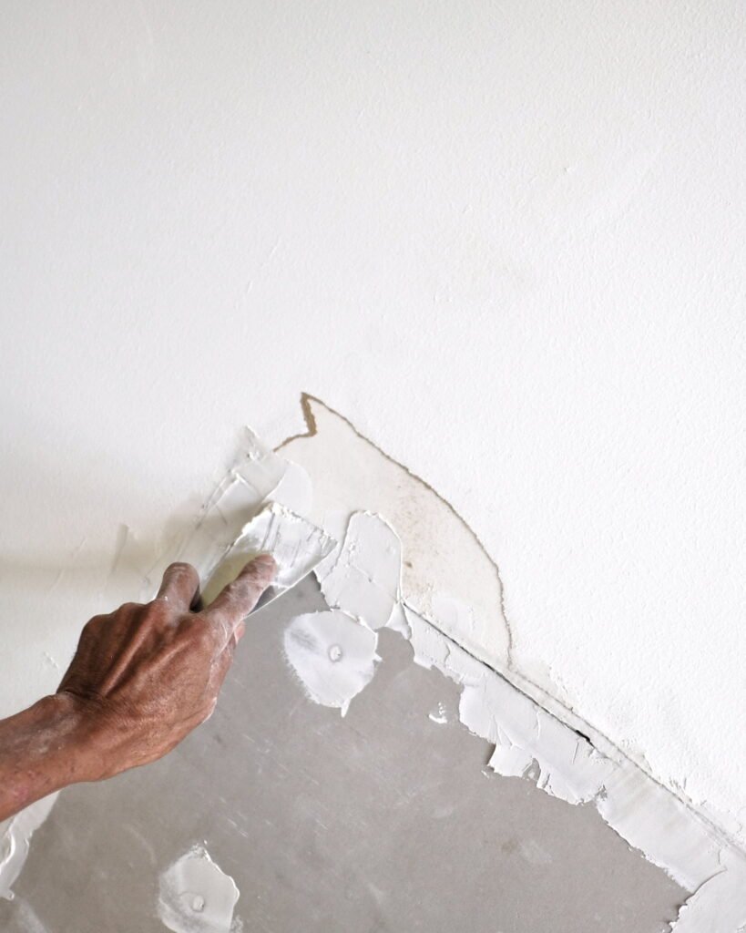 Close-up of damaged drywall being patched and smoothed by hand, showcasing Alcord Construction’s clean, precise wall repair and interior restoration work in Middle Georgia.